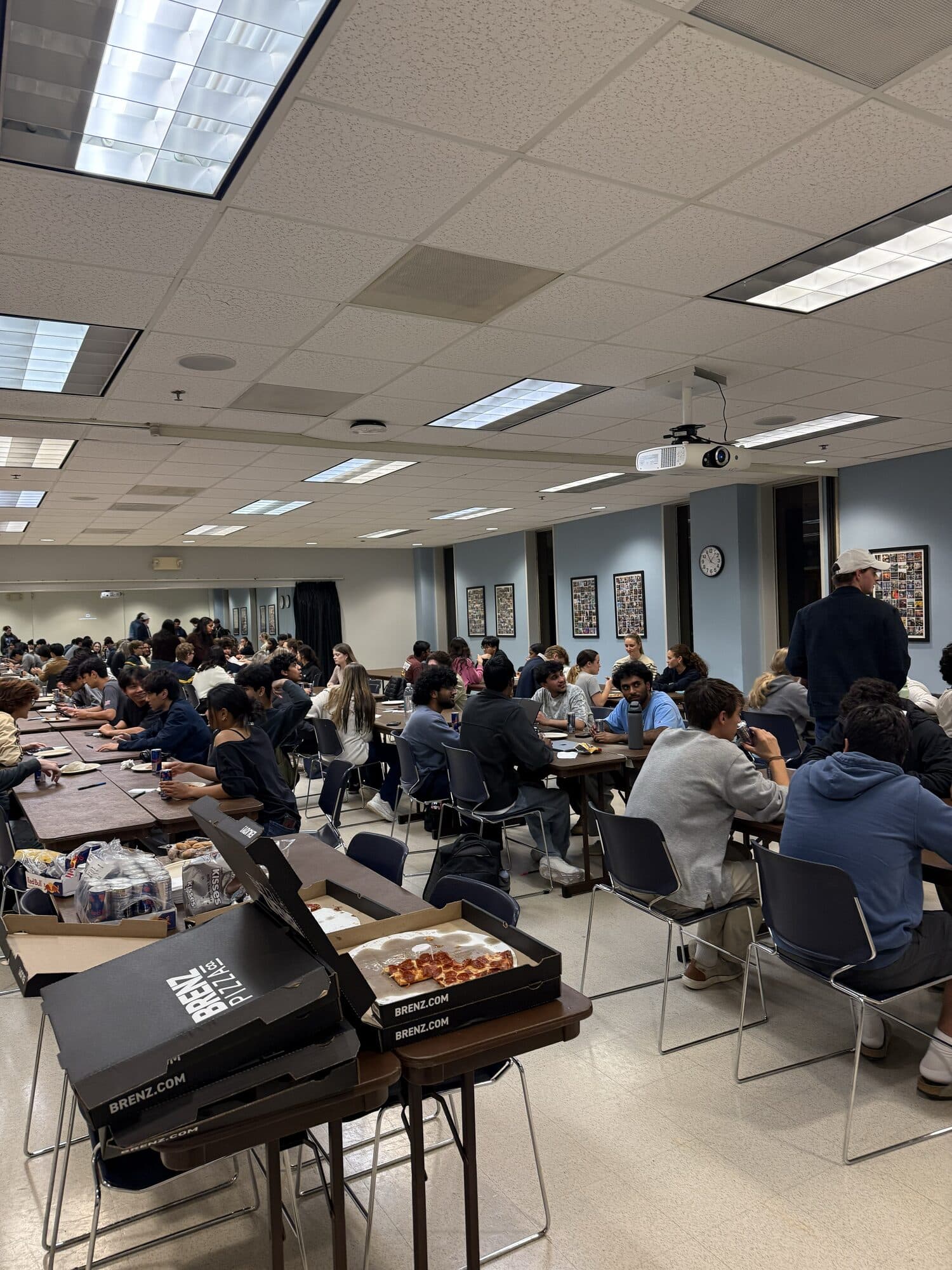 Trivia Night: a packed room of students at tables, seen past a stack of pizza boxes.